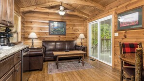 A cozy cabin interior with a wooden ceiling, a leather sofa, a coffee table, and a dining table.