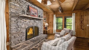 Ein Kamin aus Stein mit Feuer, Holzwände, ein kariertes Sofa und ein Fenster mit Jalousien.