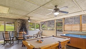 A pool table with a stone fireplace, wooden chairs, and a ceiling fan in a covered outdoor area. - Smoky Cove: Gorgeous, Pet Friendly Cabin located only 1 mile from Gatlinburg City limits! (Sevierville/ Pittman Center)