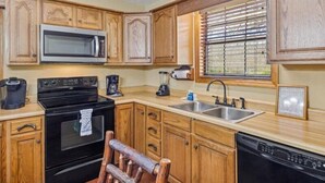 A kitchen with wooden cabinets, a microwave, a stove, a sink, and a dishwasher. - Smoky Cove: Gorgeous, Pet Friendly Cabin located only 1 mile from Gatlinburg City limits! (Sevierville/ Pittman Center)