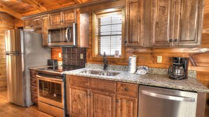 A kitchen with wooden cabinets, stainless steel appliances, granite countertops, and a window with blinds.