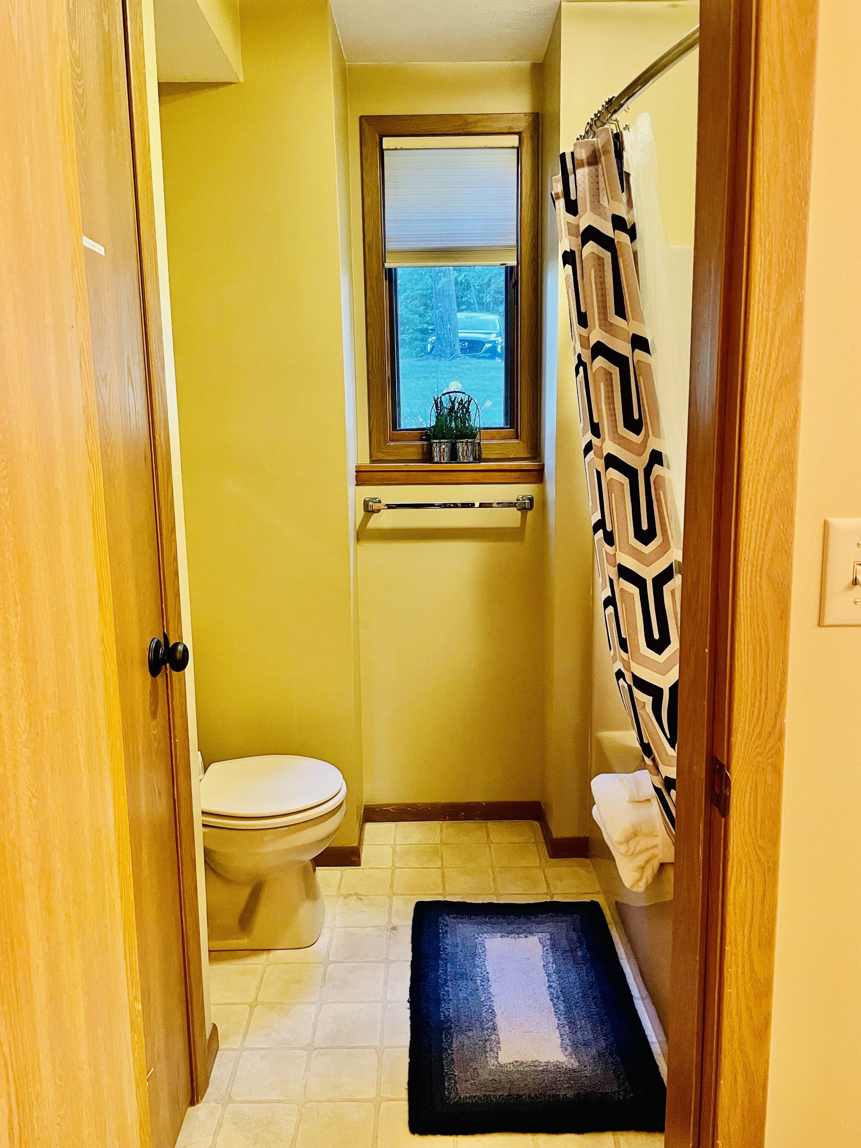 A small bathroom with a toilet, a window, a towel rack, and a shower curtain.
