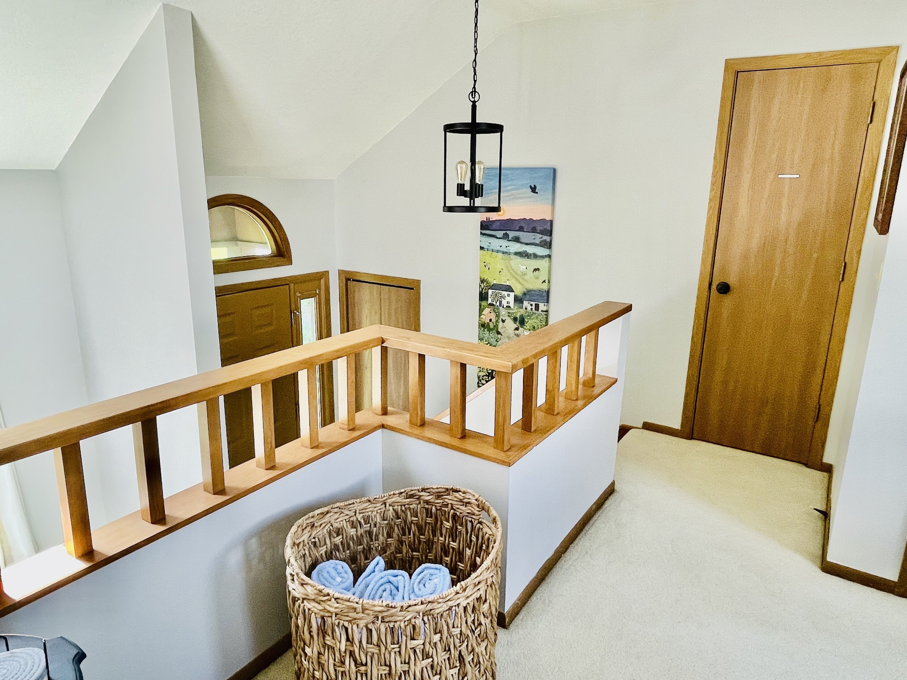 A staircase with wooden railings, a wicker basket with towels, a hanging light fixture, and a door.