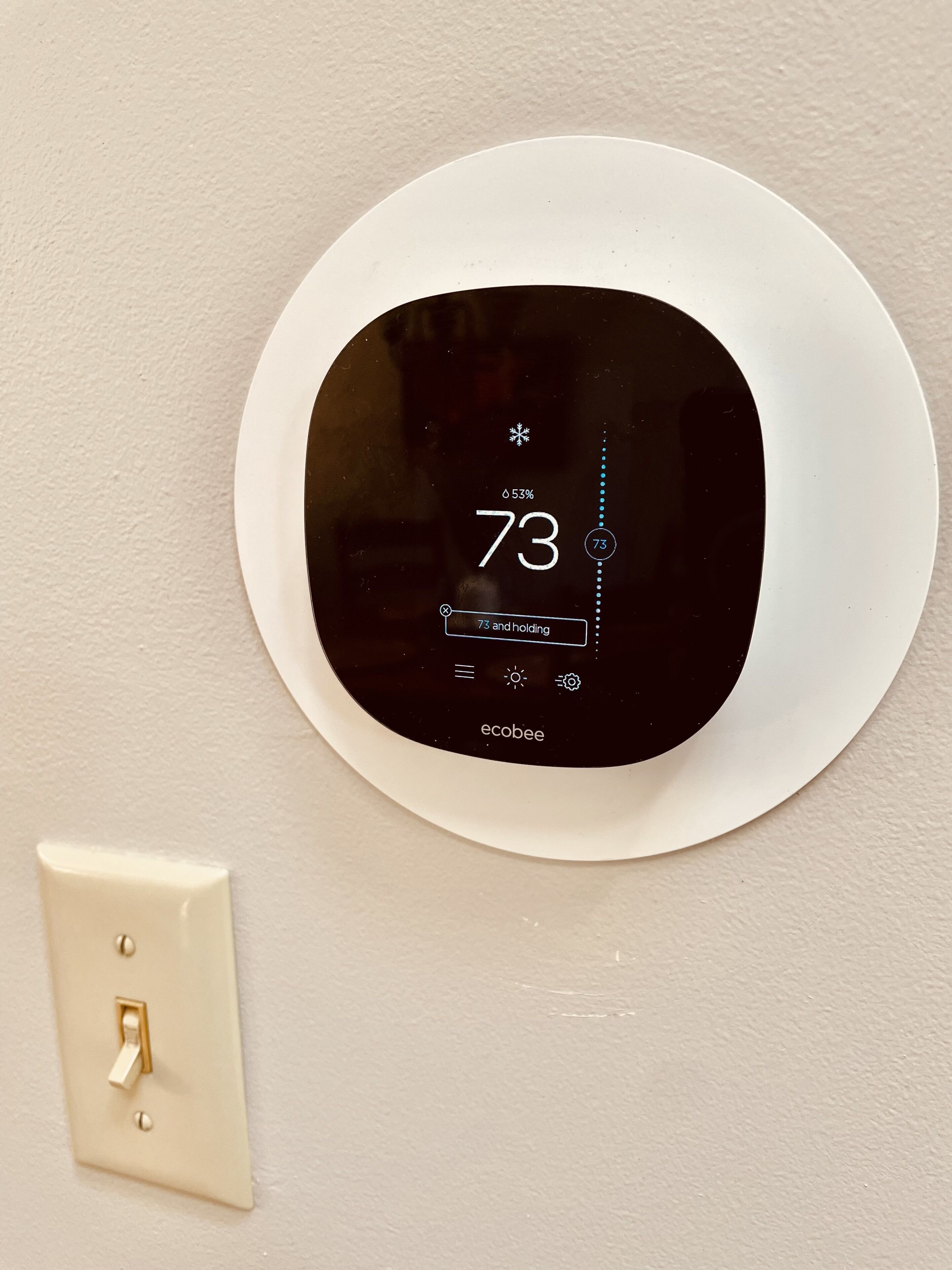 A thermostat with a digital display indicating a temperature of 73 degrees and a humidity level of 53%.