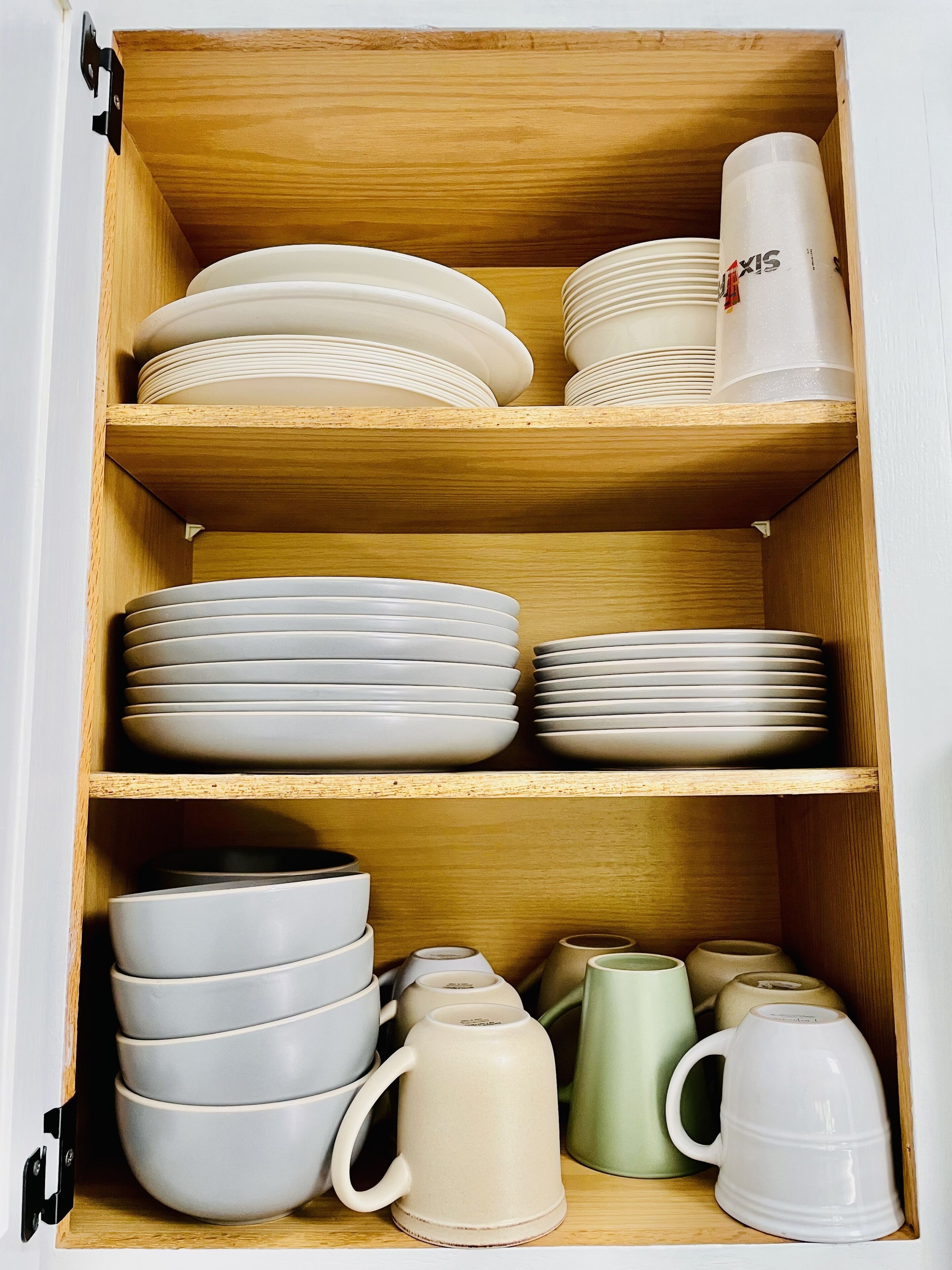 Ein Holzschrank mit mehreren Regalen, gefüllt mit gestapelten Tellern, Schüsseln und Tassen.