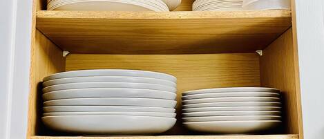 A wooden cabinet with multiple shelves containing stacked plates, bowls, and mugs.
