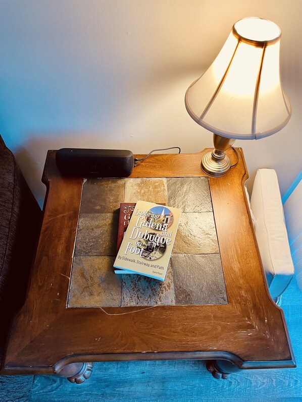 A wooden side table with a book titled "Exploring Galena and Dubuque on Foot" by David Ryan, a lamp, and a power strip.