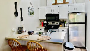 A compact kitchen with white cabinets, a black microwave, a stainless steel refrigerator, and a small island with chairs. - Charming, Farmhouse Chic, Cozy|Fireplace|12 Min to Town|Beautiful View (Galena)