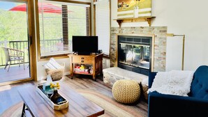 A living room with a fireplace, a television, a balcony with a chair, and a painting of a rooster. - Charming, Farmhouse Chic, Cozy|Fireplace|12 Min to Town|Beautiful View (Galena)