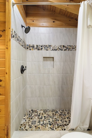 A shower with mosaic tiles, wooden ceiling, and a white curtain.