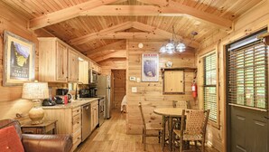 Interior de una cabaña de madera con cocina, comedor y un sofá.
