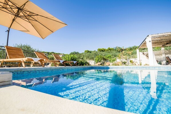 A clear blue pool with wooden lounge chairs and a large umbrella.