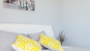 A bed with striped bedding and two yellow pillows, a white headboard, and a wall-mounted picture of a bridge and building.