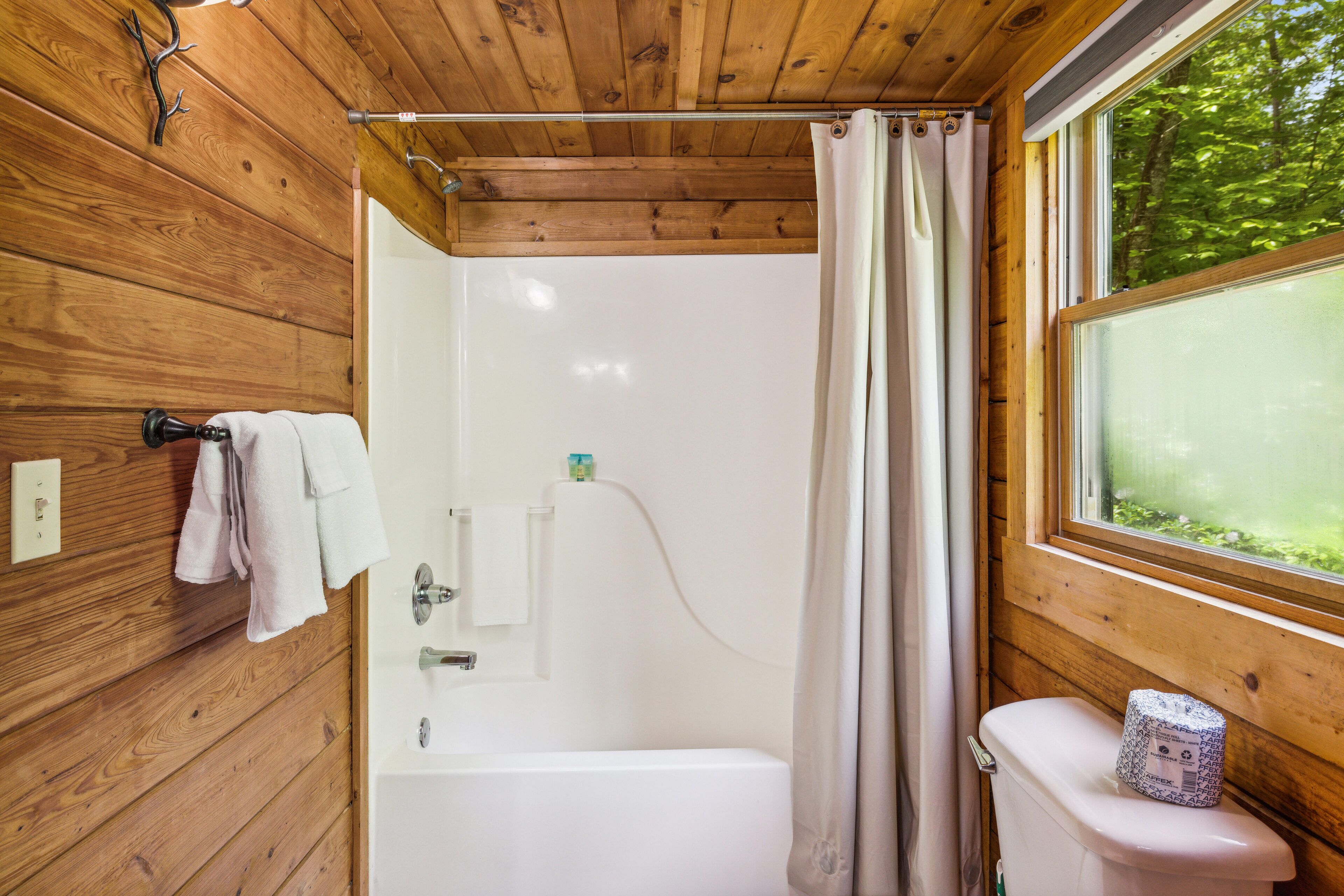 A wooden cabin bathroom with a bathtub, toilet, and window.