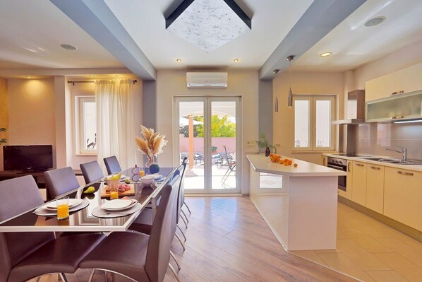 A modern kitchen with a central island, a dining area with a glass table, and a large sliding glass door leading to an outdoor patio.