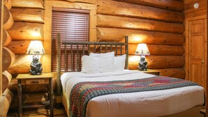 Een kamer in chaletstijl met een houten bed, twee nachtkastjes met lampen en een raam met jaloezieën.