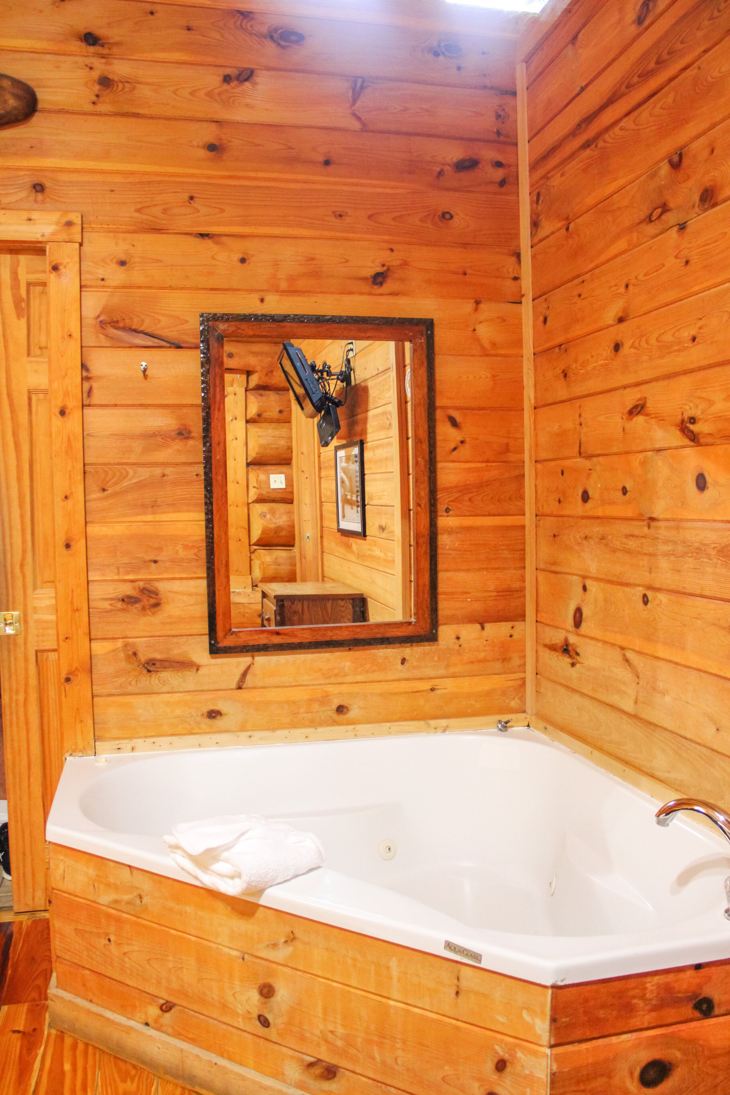 Una cabaña de madera con una bañera de madera, un espejo y una toalla.