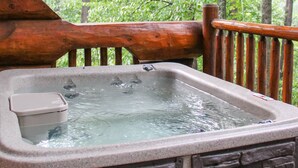 Een houten terras met een jacuzzi, omgeven door bomen.