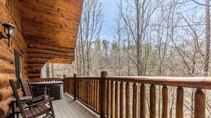 A wooden deck with a railing, a rocking chair, and a stone fireplace.