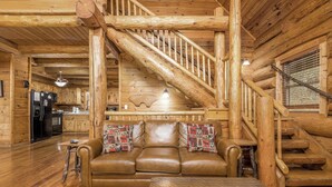 A log cabin interior with a wooden staircase, a leather sofa, and a dining table.
