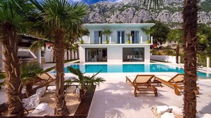 A modern villa with a pool, surrounded by palm trees and a mountainous backdrop.