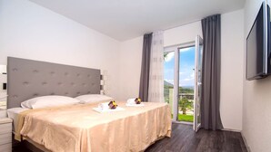 A hotel room with a large bed, a flat-screen TV, and a balcony with a view of the outdoors.