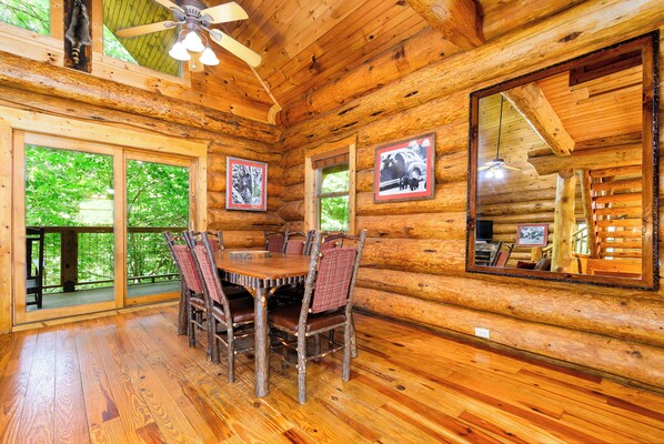 Interior de una cabaña de madera con una mesa de comedor, sillas y ventanas amplias.