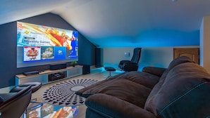 A modern living room with a large flat-screen TV mounted on the wall, a comfortable brown sofa, a black gaming chair, and a patterned rug on the floor. - Villa Nedy - Four Bedroom Villa, Sleeps 8 (Zakucac)