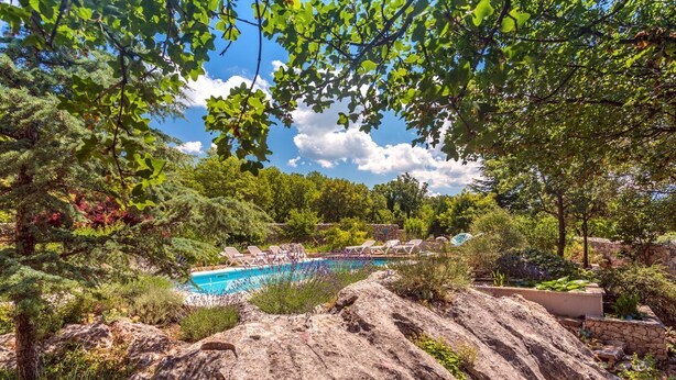 Ein Pool, umgeben von Steinen und Bäumen, mit Liegestühlen und einer Steinmauer im Hintergrund.