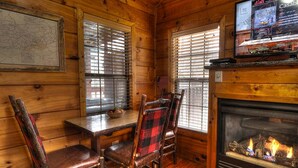 A wooden cabin interior with a fireplace, wooden walls, and a dining table with chairs.