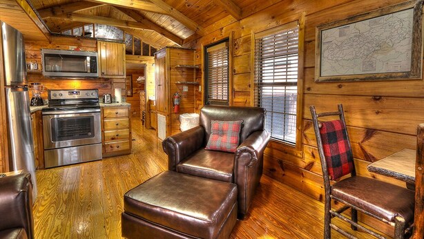 A log cabin interior with a kitchen, a leather armchair, and a dining area.