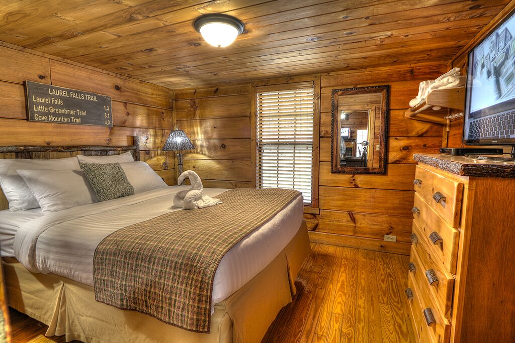 Une chambre rustique en bois, avec un lit, une commode, une télévision et un panneau indiquant les différents sentiers de randonnée.