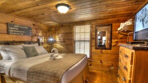 A wooden cabin room with a bed, a dresser, a television, and a sign listing trails.