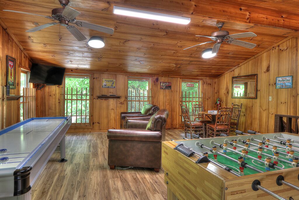 A wooden-floored room with a foosball table, a pool table, and a leather couch.