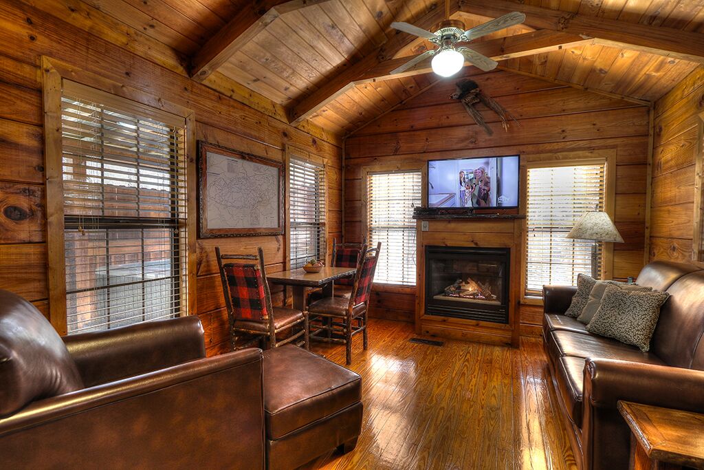 Un interior de cabaña acogedor con detalles de madera, una chimenea, un televisor y muebles de cuero.