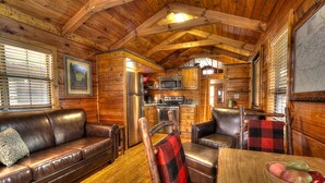 L’intérieur chaleureux de ce chalet est agrémenté de boiseries, d’une petite cuisine, d’un coin repas avec une table et des chaises, ainsi que d’un canapé en cuir.