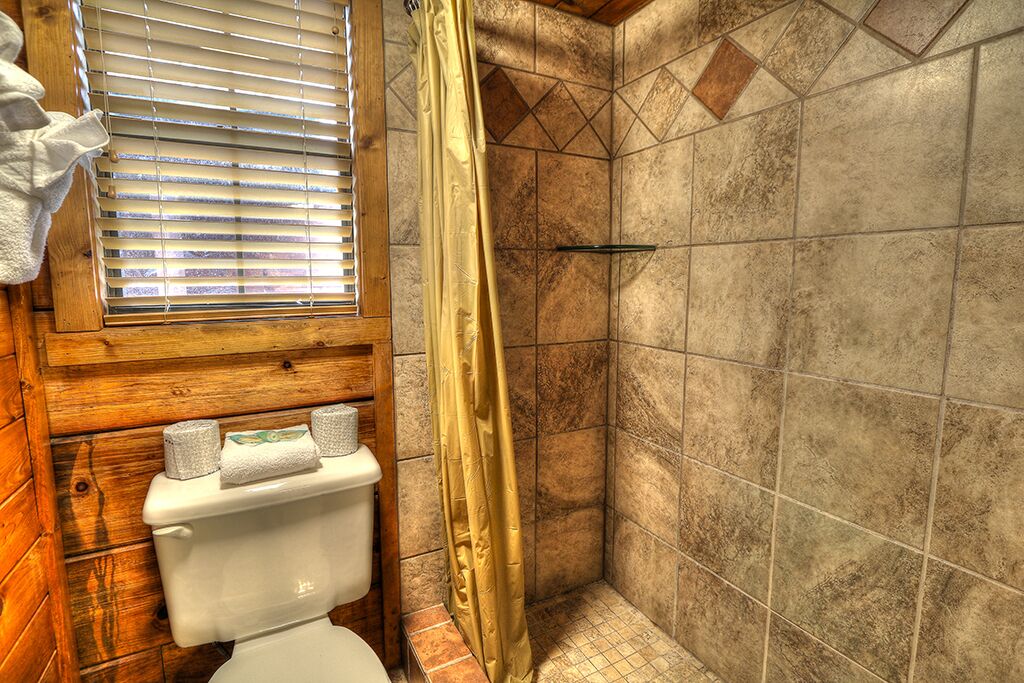Un baño con inodoro de madera, ducha con cortina amarilla y ventana con persianas.