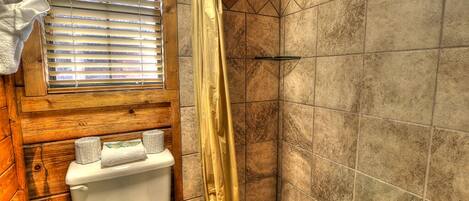 Un baño con inodoro de madera, ducha con cortina amarilla y ventana con persianas.