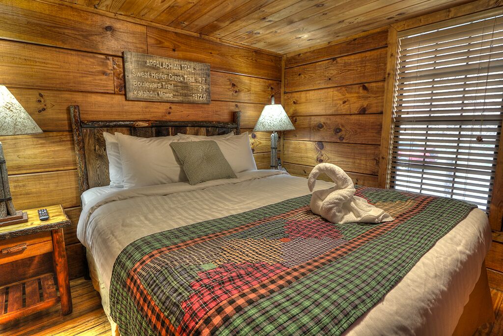 Ein schlicht eingerichtetes Schlafzimmer im Holzchalet-Stil mit einem Bett, zwei Nachttischlampen, einer Steppdecke und einem Schild an der Wand mit Wanderwegen.