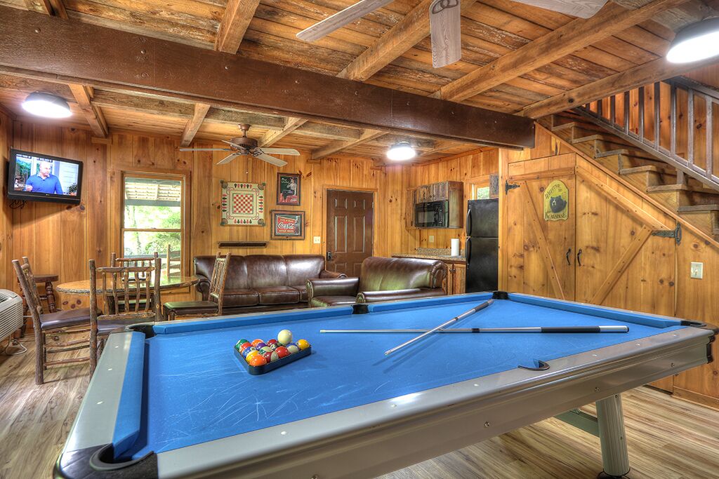 A pool table with balls, a television, and a ceiling fan in a wooden room with a staircase.