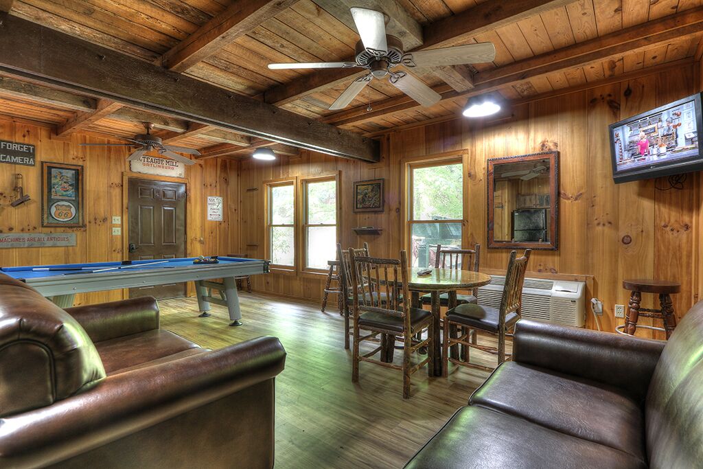 Un intérieur en bois avec une table de billard, des sièges en cuir et un ventilateur de plafond.