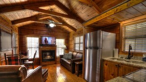 L’intérieur d’une cabane en rondins comprend un salon, une cheminée, un canapé et un coin cuisine.