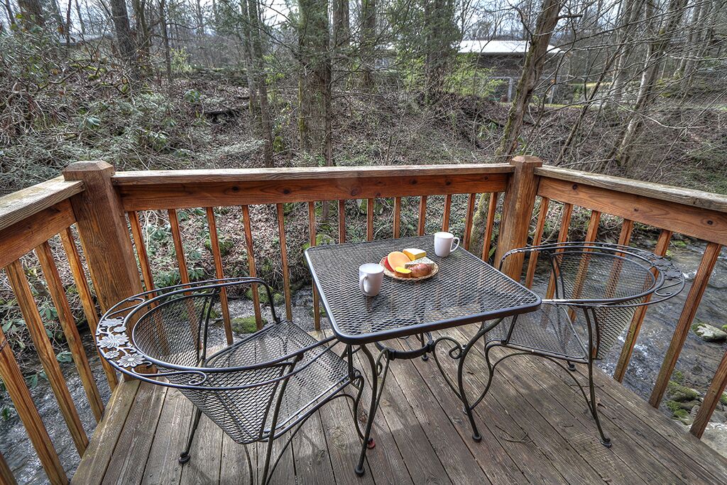 A wooden deck with a metal table and chairs, surrounded by a wooden railing.