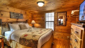 Een knus houten kamer met een bed, een dressoir, een televisie en een raam.
