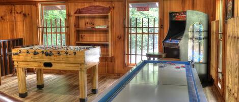 A wooden-floored room with a foosball table, a pool table, and a vintage arcade machine.