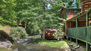 Een rustieke chalet met een houten terras en een beekje dat door de tuin stroomt.