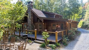 A rustic log cabin with a stone chimney, wooden deck, and outdoor seating area.