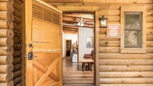A wooden log cabin entrance with a large wooden door, a ceiling fan, and a sign warning about hot water.
