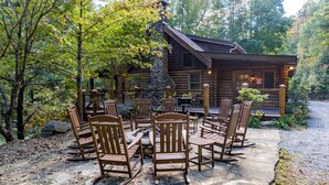 A wooden cabin with a stone fireplace, surrounded by a patio with wooden chairs and tables.