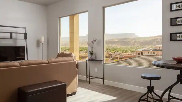 A modern living room with a large window, a sofa, a coffee table, and a TV. - Amazing VIEWS, NEW quiet home, bonus Fitness Room! (Hurricane)